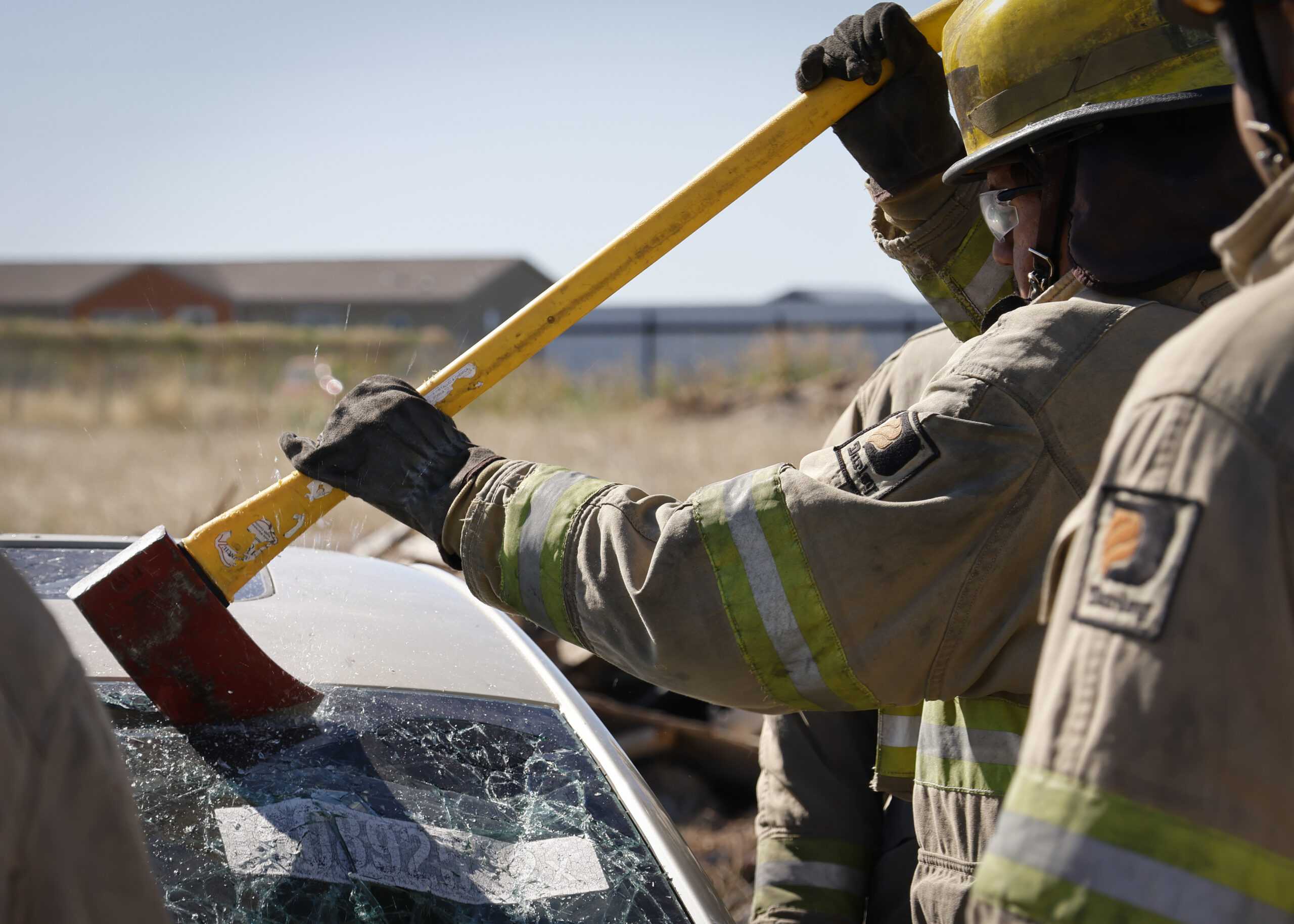 A student uses an ax to break a car windshield away from its frame while training on vehicle extraction. Photo by Natalia Edwards.